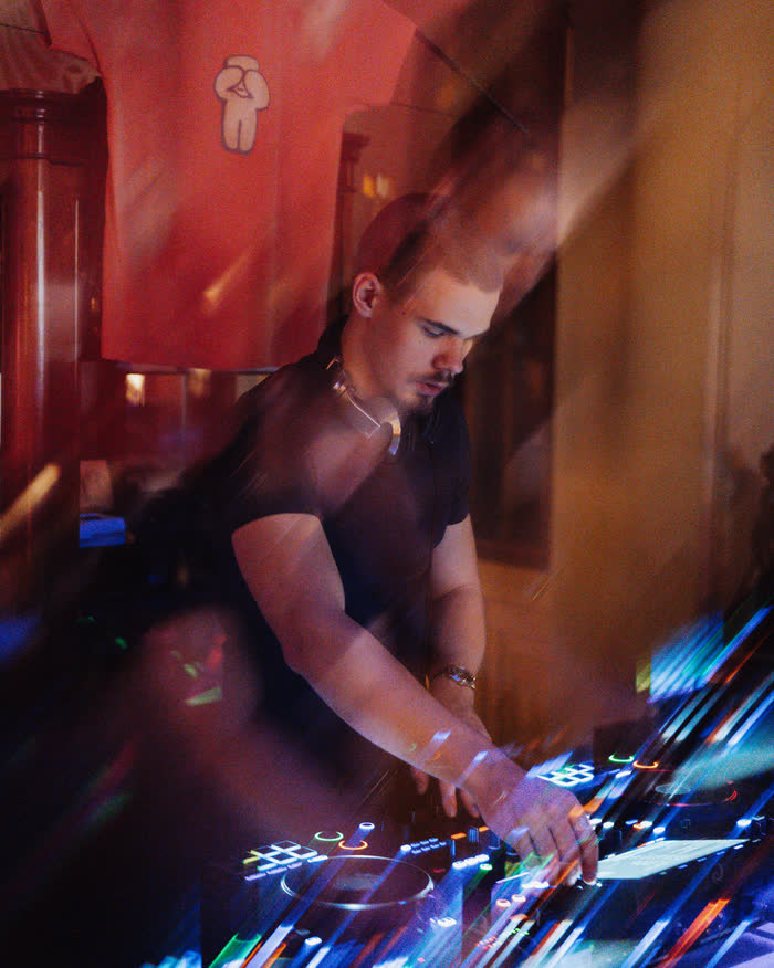 Kaur Nellis behind the decks, hands on the controller, light streaking across the booth in red and blue.