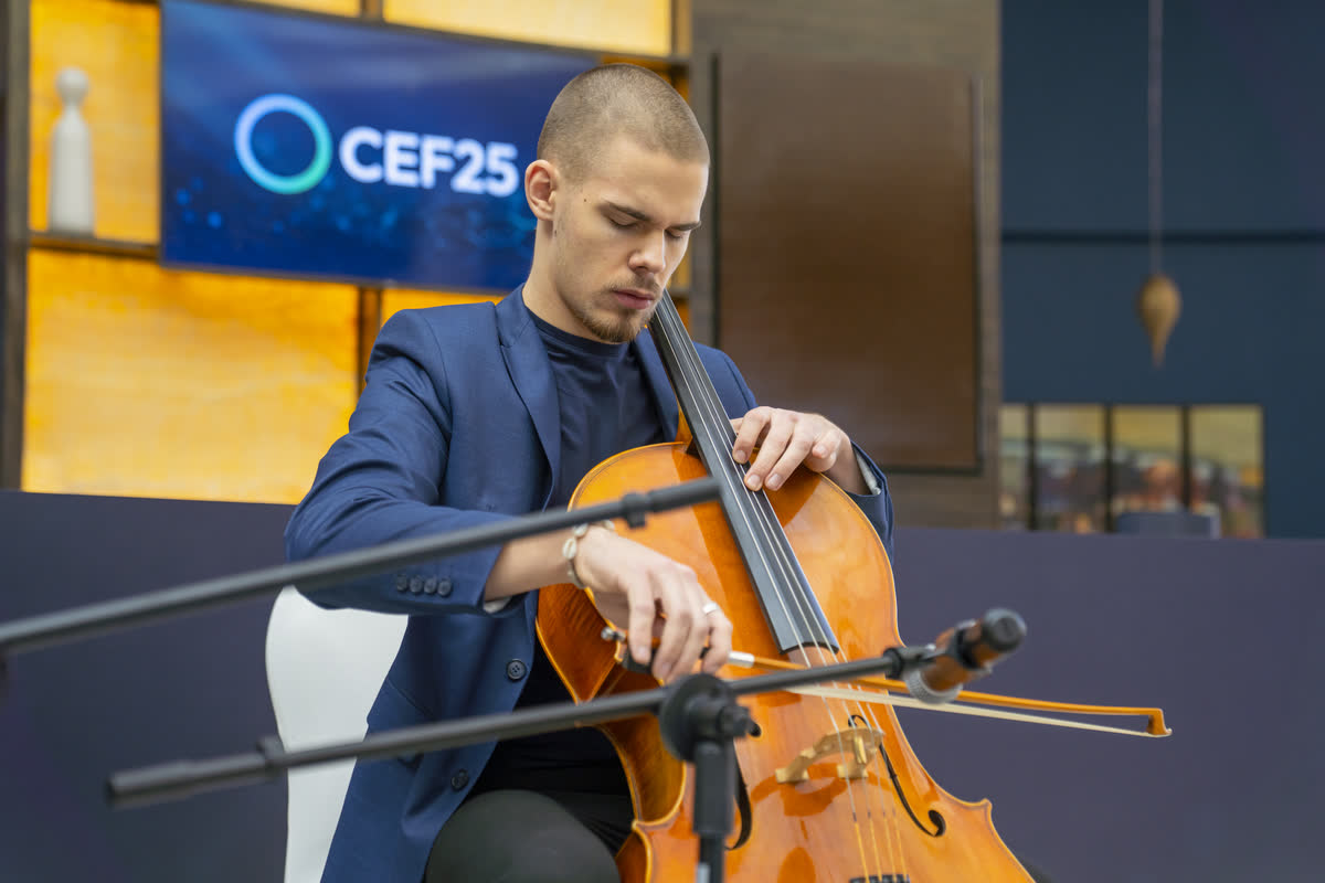 Kaur Nellis playing cello on stage at the Circular Economy Forum in Riyadh, lit by the venue's gold wall panels.