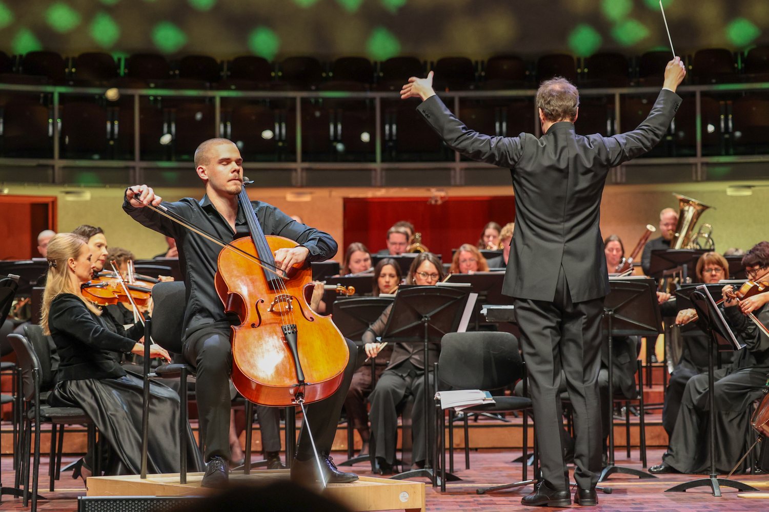 Kaur Nellis playing as soloist on a raised platform in front of Pärnu City Orchestra, the conductor with both arms raised beside him.